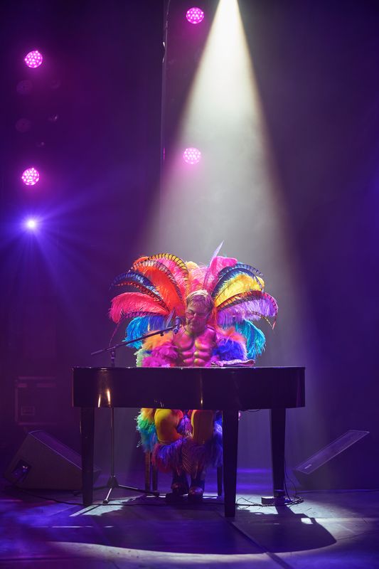 A man in a vibrant outfit performs on stage during "The Rocket Man" Elton John tribute show