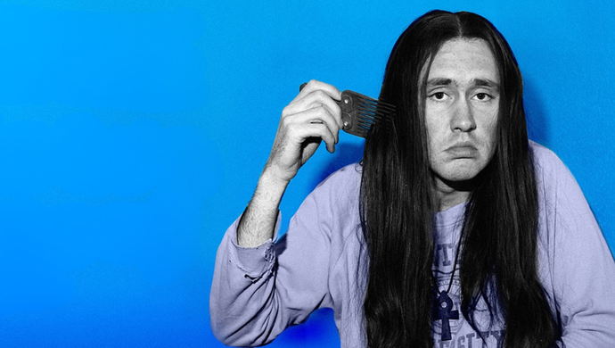A man with long hair, Nigel Planer, is combing his hair with a focused expression