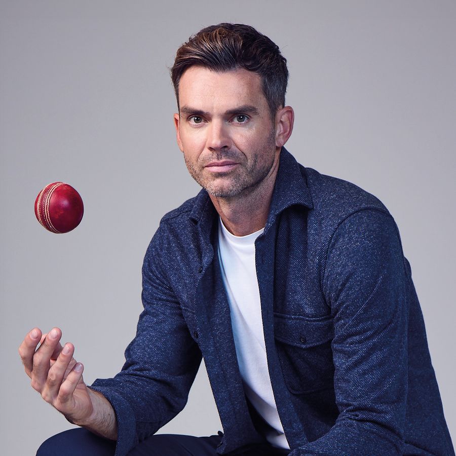 Cricket legend Jimmy Anderson sits on a chair, casually throwing a cricket ball in the air